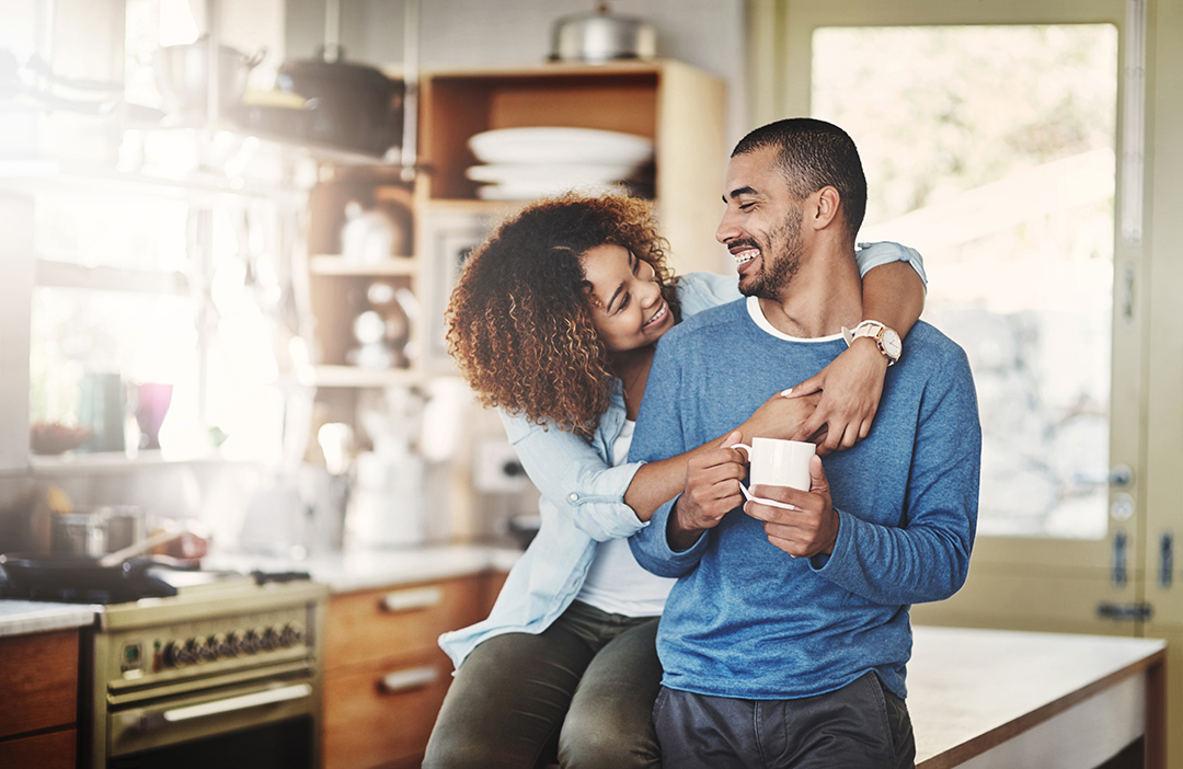 Love, coffee and happy couple in kitchen, morning hug in home with smile, hugging and healthy relationship. Happiness, man and woman embrace with affection, romance and young people in apartment.